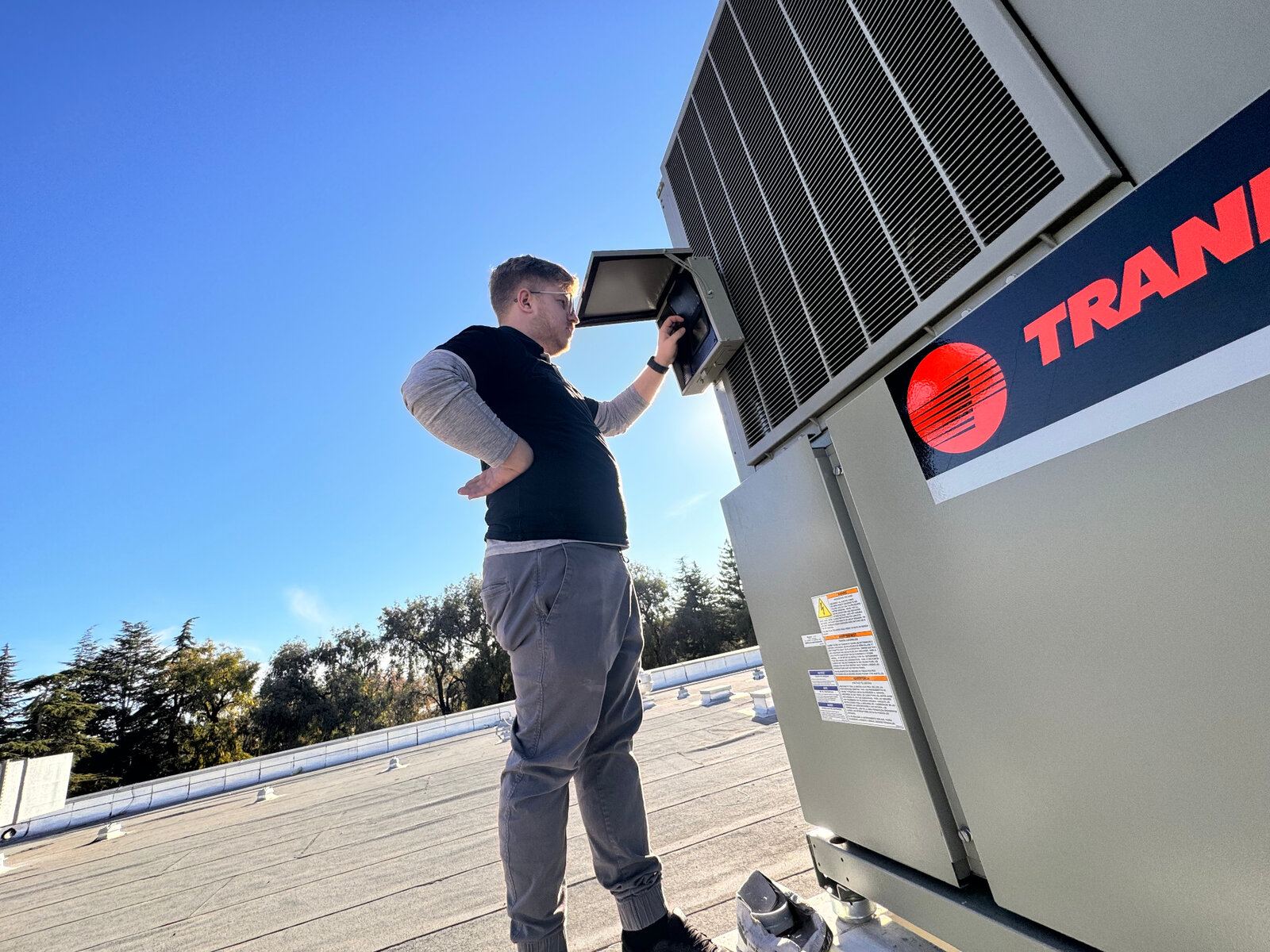 ABC Service technician opening the control panel on a rooftop Trane packaged heat pump during a scheduled maintenance visit in the Bay Area.
