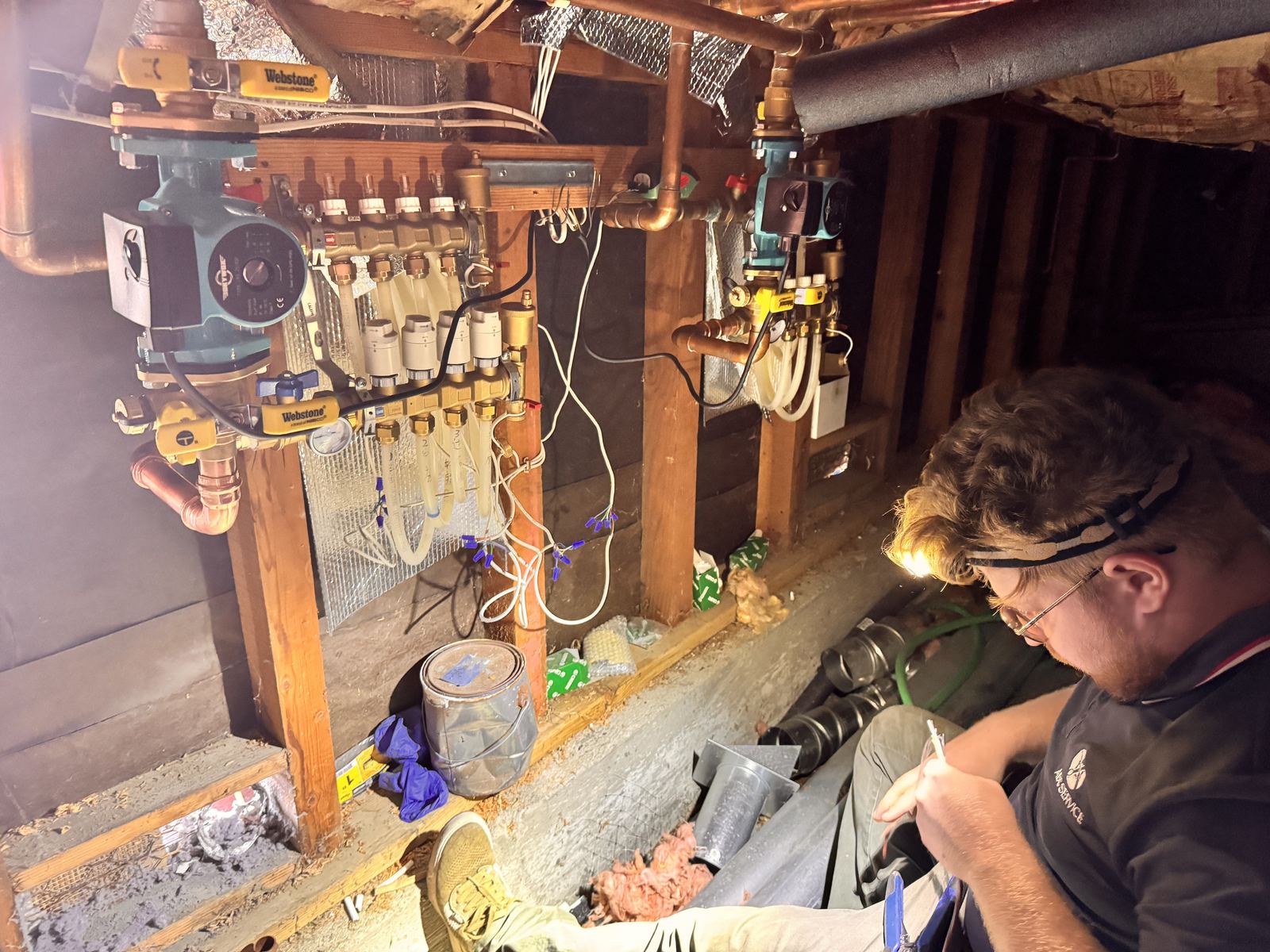ABC Service technician diagnosing a hydronic mechanical room with manifold, ECM circulators, copper piping, and a Navien condensing boiler.