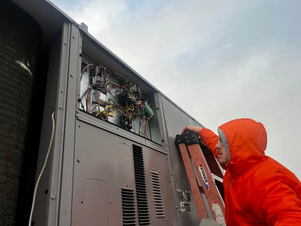 ABC Service technician diagnosing the open control panel of a commercial rooftop packaged HVAC unit.
