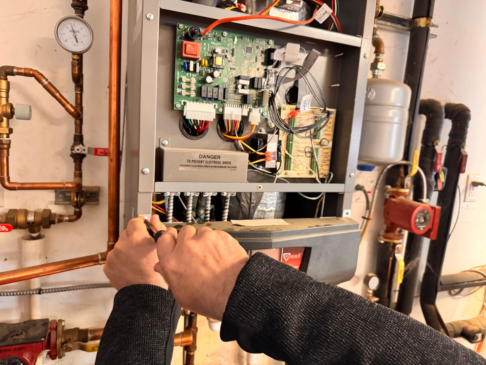 ABC Service technician servicing a modern condensing boiler control board with copper near-boiler piping, expansion tank, and zone circulator in a Bay Area mechanical room.